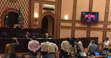 Speaker Abdulla Maseeh addresses the first sitting of 2017's third term of the parliament from his elevated seat behind a wooden "wall", while opposition lawmakers protest and call on him to step down.